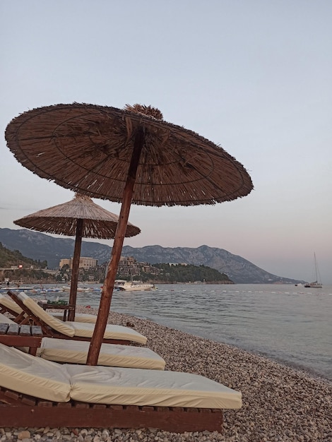 Parasols de plage en paille d'été avec transats sur la plage de galets en soirée