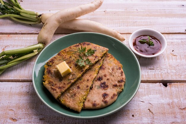 Paratha farci au Daikon ou au radis ou au Mooli servi dans une assiette avec du beurre et du ketchup aux tomates, sur fond coloré ou en bois. mise au point sélective