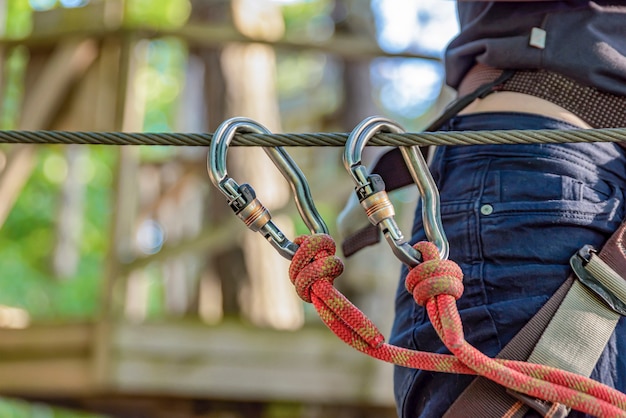 Photo parc aventure forestier. la femme attache son mousqueton et utilise le matériel d'escalade. surmontez les obstacles dans le parc d'aventure en forêt. bannière publicitaire et endroit pour insérer du texte.