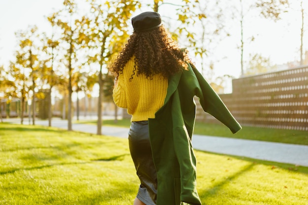 Sur le parc, l'herbe est retirée de la caméra fille aux longs cheveux bouclés dans une casquette avec un manteau jeté sur une épaule