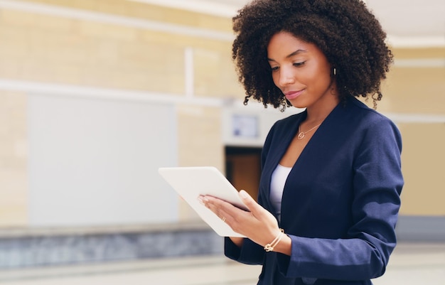 En parcourant mes e-mails Photo recadrée d'une jolie jeune femme d'affaires debout seule et utilisant une tablette au bureau pendant la journée