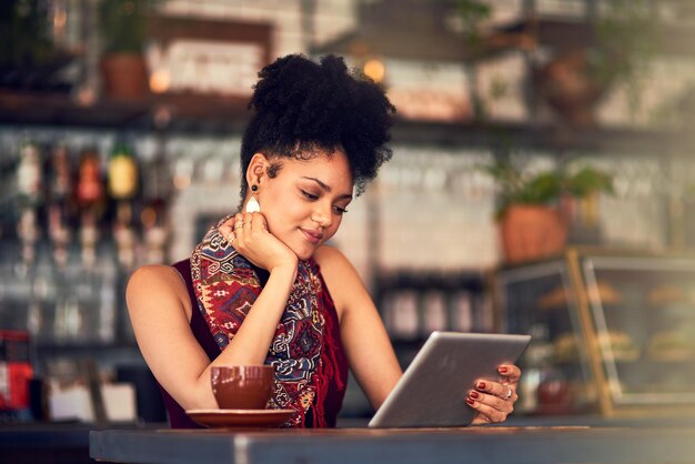 En parcourant ses flux de médias sociaux Photo recadrée d'une jolie jeune femme à l'aide d'une tablette numérique dans un café