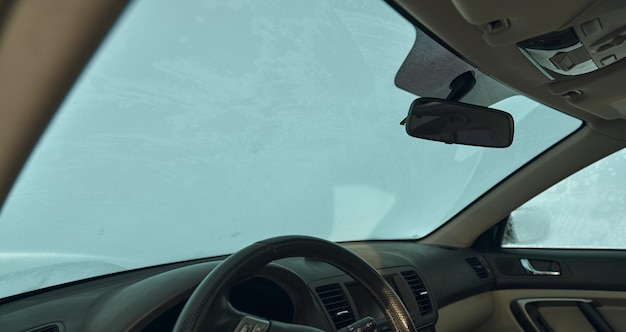 Pare-brise de voiture couvert de glace Intérieur d'une voiture pendant l'hiver Assis dans la voiture sous la neige pendant les chutes de neige