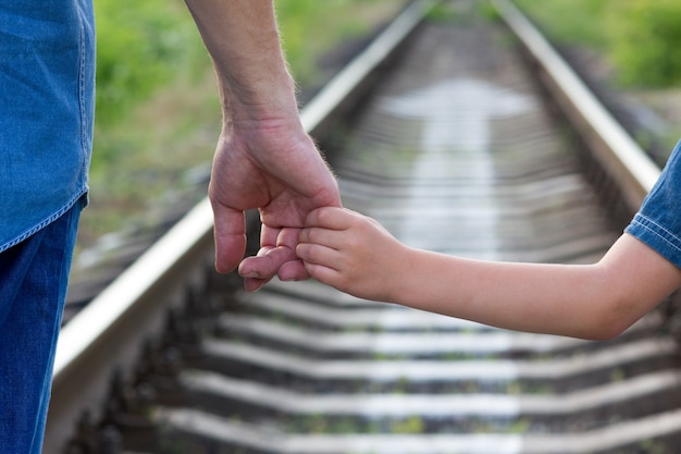 Le parent de concept tient la main d'un petit enfant et d'un chemin de fer et d'une direction