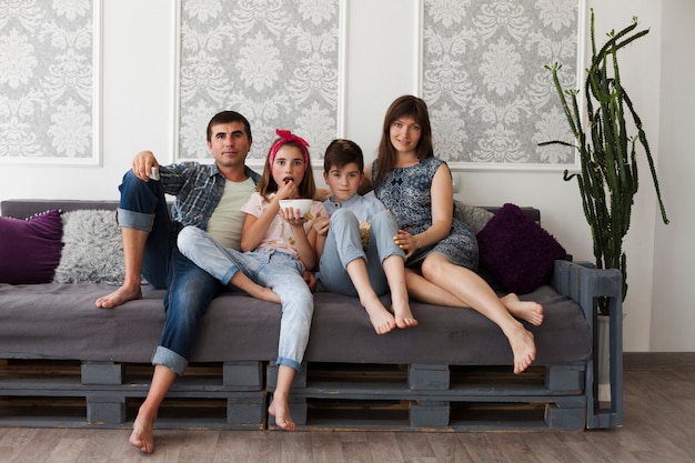 Photo parent et leurs enfants assis ensemble sur le canapé en regardant la caméra