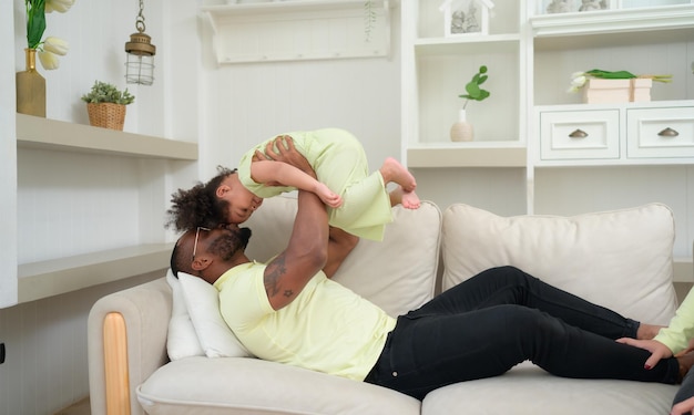 Un parent s'amuse avec sa fille en vomissant et en la soulevant pendant que la mère est à côté.