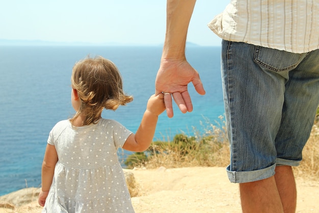 Le parent tient la main de l'enfant sur la mer en été