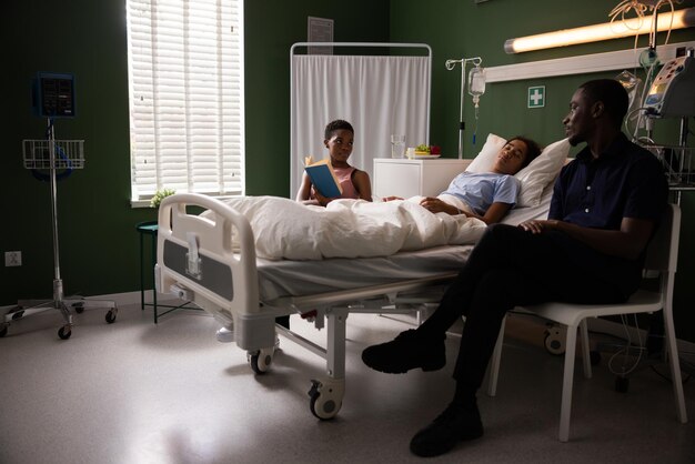 Des parents africains soutiennent leur enfant à l'hôpital. La mère lit le livre pendant que l'enfant dort.