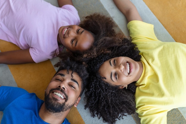 Des parents afro-américains affectueux et une jolie fille riant allongés sur le sol ensemble une famille métisse heureuse avec des liens d'enfants s'amusant profiter de moments amusants dans la chambre vue de dessus d'en haut