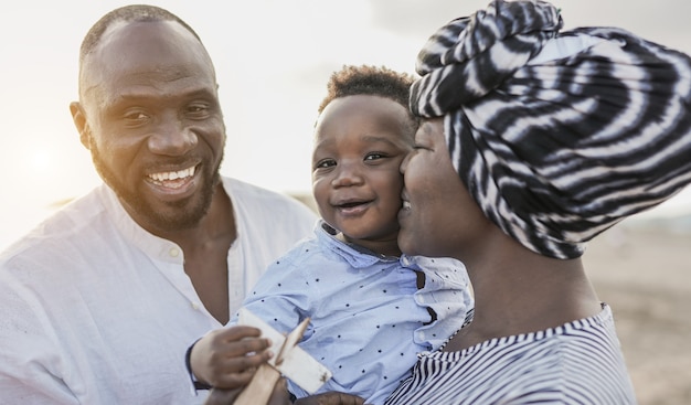 Les parents afro-américains profitent des vacances d'été sur la plage avec un enfant en bas âge - Amour familial - Mère embrassant un bébé mignon en plein air