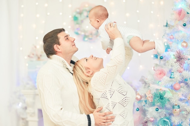 Des parents aimants qui jouent avec leur bébé debout dans le salon festif. le concept de Noël