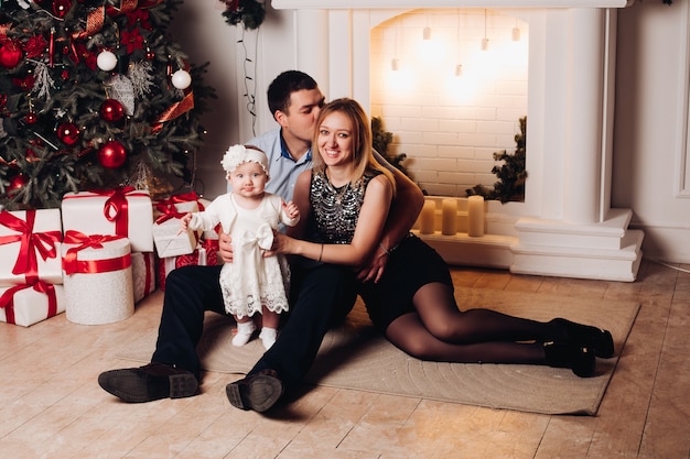 Parents assis sur le sol avec l'enfant près de sapin de Noël.