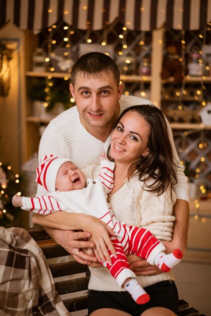 Les parents célèbrent le nouvel an à la maison avec un petit enfant assis près de l'arbre de Noël et tenant le b...