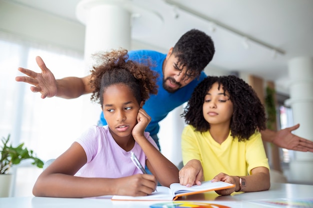 Parents criant après leur fille tout en faisant ses devoirs à la maison Jeune père et mère aidant sa fille à étudier dans le salon