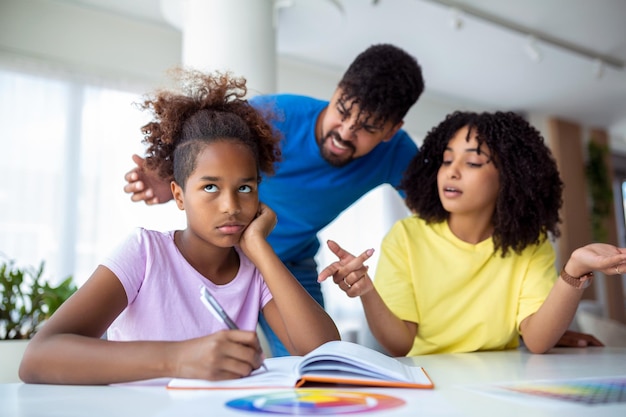 Parents criant après leur fille tout en faisant ses devoirs à la maison Jeune père et mère aidant sa fille à étudier dans le salon