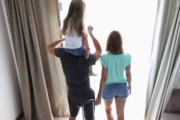 Les parents et l'enfant se tiennent dans les chambres d'hôtel et regardent par la fenêtre