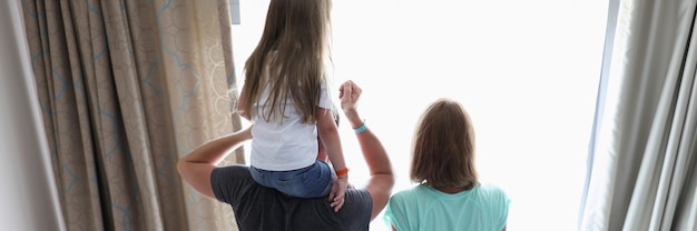 Les parents et l'enfant se tiennent dans les chambres d'hôtel et regardent par la fenêtre