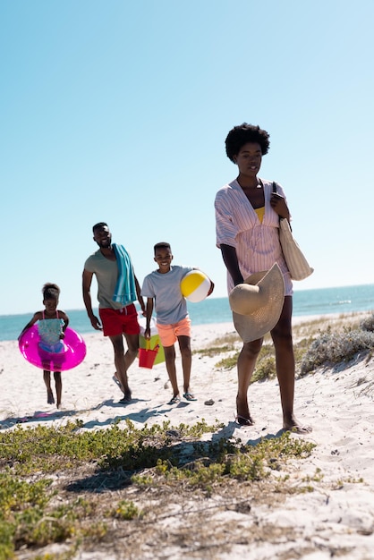 Parents et enfants afro-américains marchant sur une plage de sable contre un ciel bleu clair pendant les vacances. Espace de copie, inchangé, famille, ensemble, enfance, pique-nique, nature, vacances, plaisir, été.