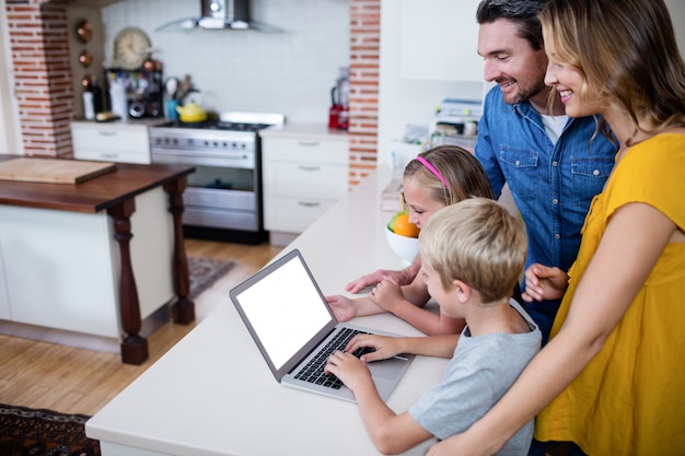 Parents et enfants utilisant un ordinateur portable dans la cuisine