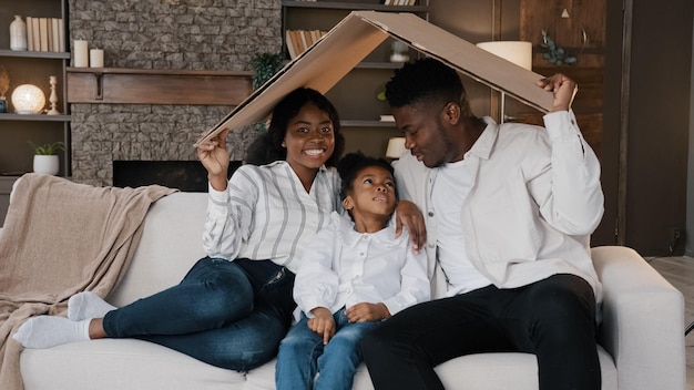 Photo parents de famille afro-américains avec fille petite fille enfant adopté assis sur un canapé sous carton