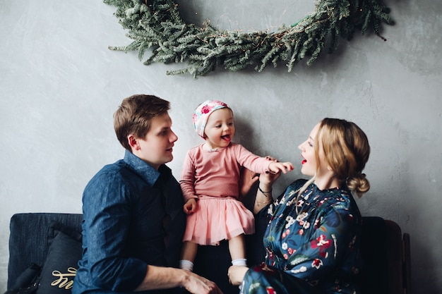 Parents et fille assise sur le canapé sous la grande couronne de sapin.