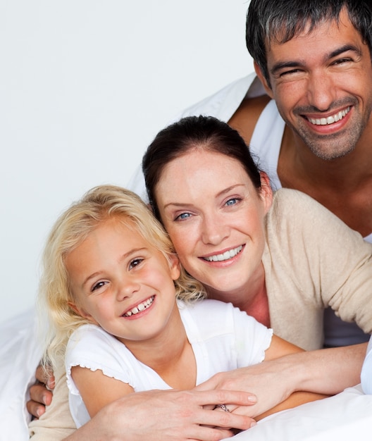 Parents et fille sur le lit en souriant à la caméra