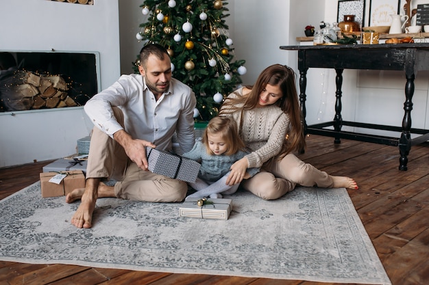 Parents et fille sur le sol près d'un arbre de Noël à la maison