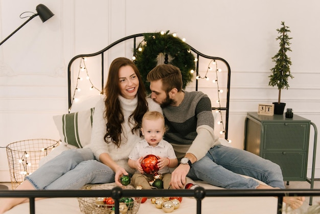 Les parents heureux jouent avec le bébé sur le lit avant Noël