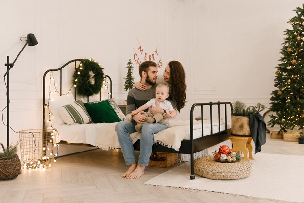 Les parents heureux jouent avec le bébé sur le lit avant Noël