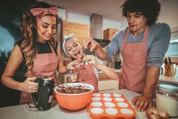 Des parents heureux et leur fille préparent des biscuits ensemble dans la cuisine. Petite fille aide ses parents avec mélangeur.