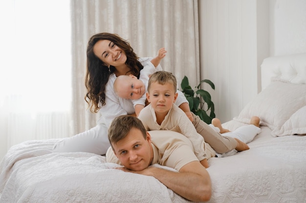 Parents jouant avec des enfants au lit dans un appartement blanc et confortable