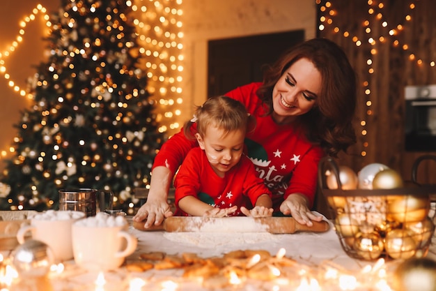 Des parents joyeux et un enfant en pyjama rouge préparent des biscuits de Noël dans la cuisine décorée