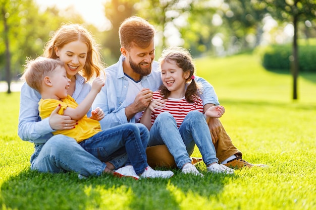 Parents joyeux souriant et jouant avec des enfants assis sur l'herbe verte par une journée d'été ensoleillée dans le parc