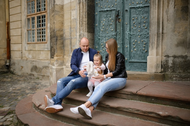 Les parents et leur fille sont assis sur les marches d'une ancienne église.