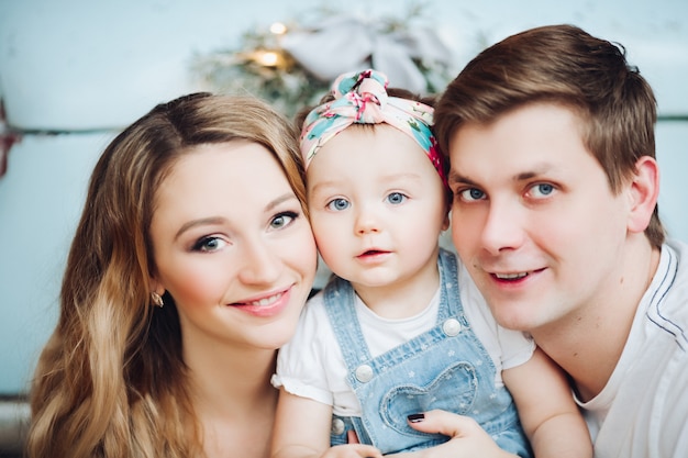 Parents à la mode tenant sur les mains petite fille mignonne, debout près de voiture rétro bleue.