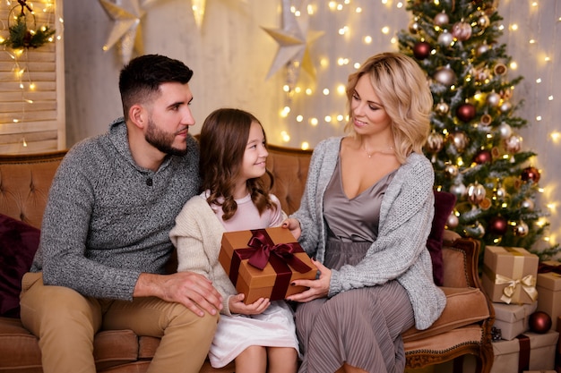 Parents offrant un cadeau à leur fille dans le salon avec un sapin de Noël décoré et des lumières