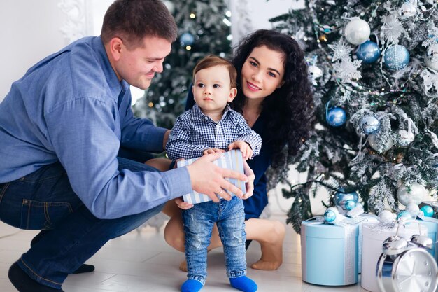 Les parents et le petit fils près de l'arbre de Noël bébé tenant un cadeau