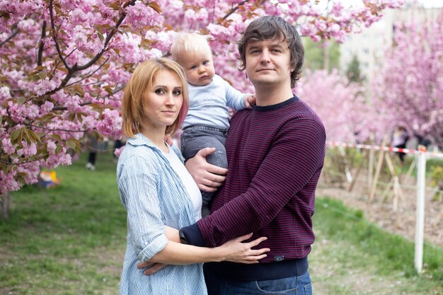 Parents et petit garçon fils s'amusant dans le parc du printemps près de l'arbre en fleurs de sakura rose Concept de printemps