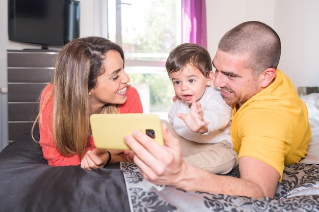 Des parents et un petit garçon utilisent un téléphone portable allongés ensemble sur le lit.