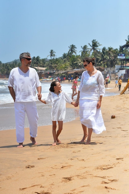 Parents avec petite fille marchant sur une plage de sable et se tenant la main