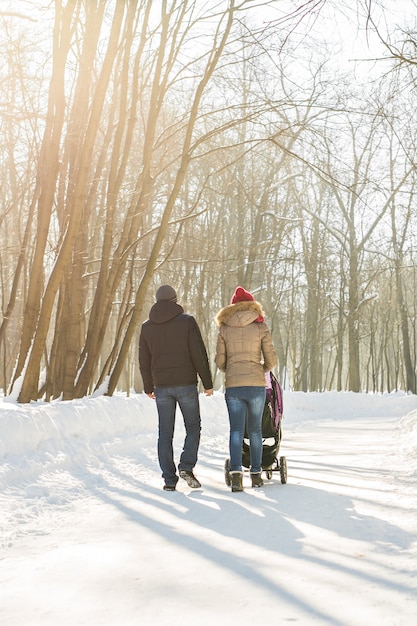 Les parents portent le bébé dans une poussette à travers la neige