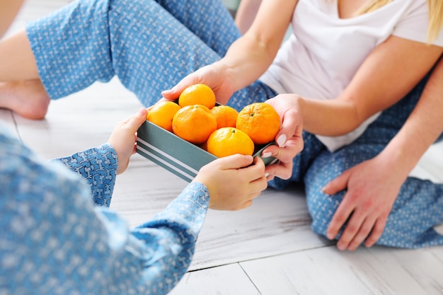 Des parents en pyjama assis par terre donnent à leur petit-fils une boîte de mandarines