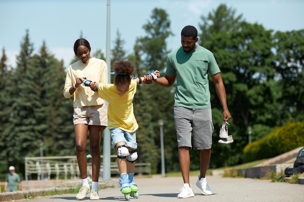 Parents tenant la main d'un enfant et lui apprenant à faire du patin à roulettes dans le parc