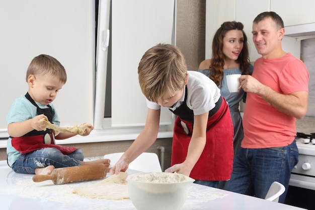 Les parents voient leurs jeunes fils, qui pétrissent la pâte sur la table de la cuisine