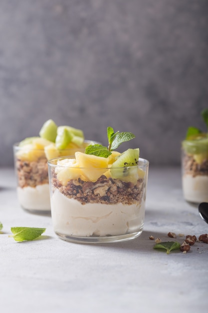 Parfait au yogourt fait maison avec granola, kiwi, ananas et noix dans un verre pour un petit déjeuner sain sur fond de béton