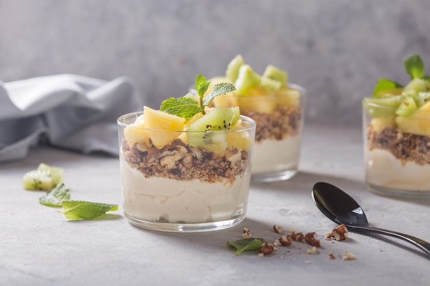 Parfait au yogourt fait maison avec granola, kiwi, ananas et noix dans un verre pour un petit déjeuner sain sur fond de béton