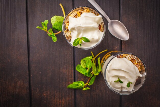 Parfait glacé à la mangue et granola à la mangue dans un verre sur un fond en bois foncé.