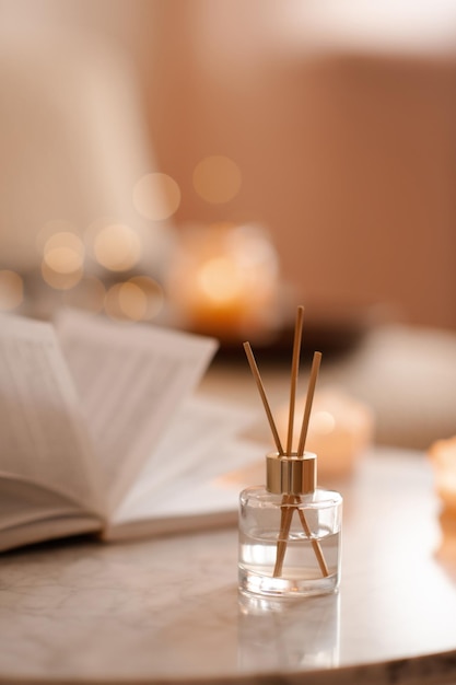 Parfum d'ambiance liquide dans un diffuseur avec un livre papier ouvert sur une table basse dans la chambre à l'intérieur en gros plan sur une bougie parfumée Ambiance chaleureuse et hygge Aromathérapie