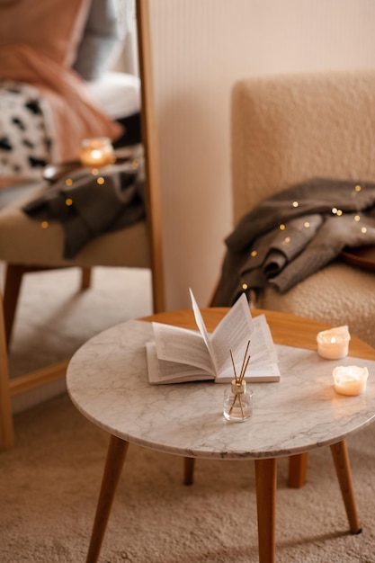 Parfum d'ambiance liquide dans un diffuseur avec un livre papier ouvert sur une table basse dans la chambre à l'intérieur en gros plan sur une bougie parfumée Ambiance chaleureuse et hygge Aromathérapie