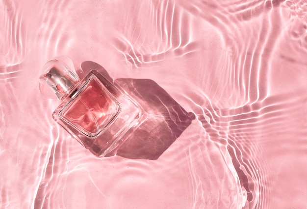 Parfum de bouteille rose transparent dans l'eau rose avec des ombres.